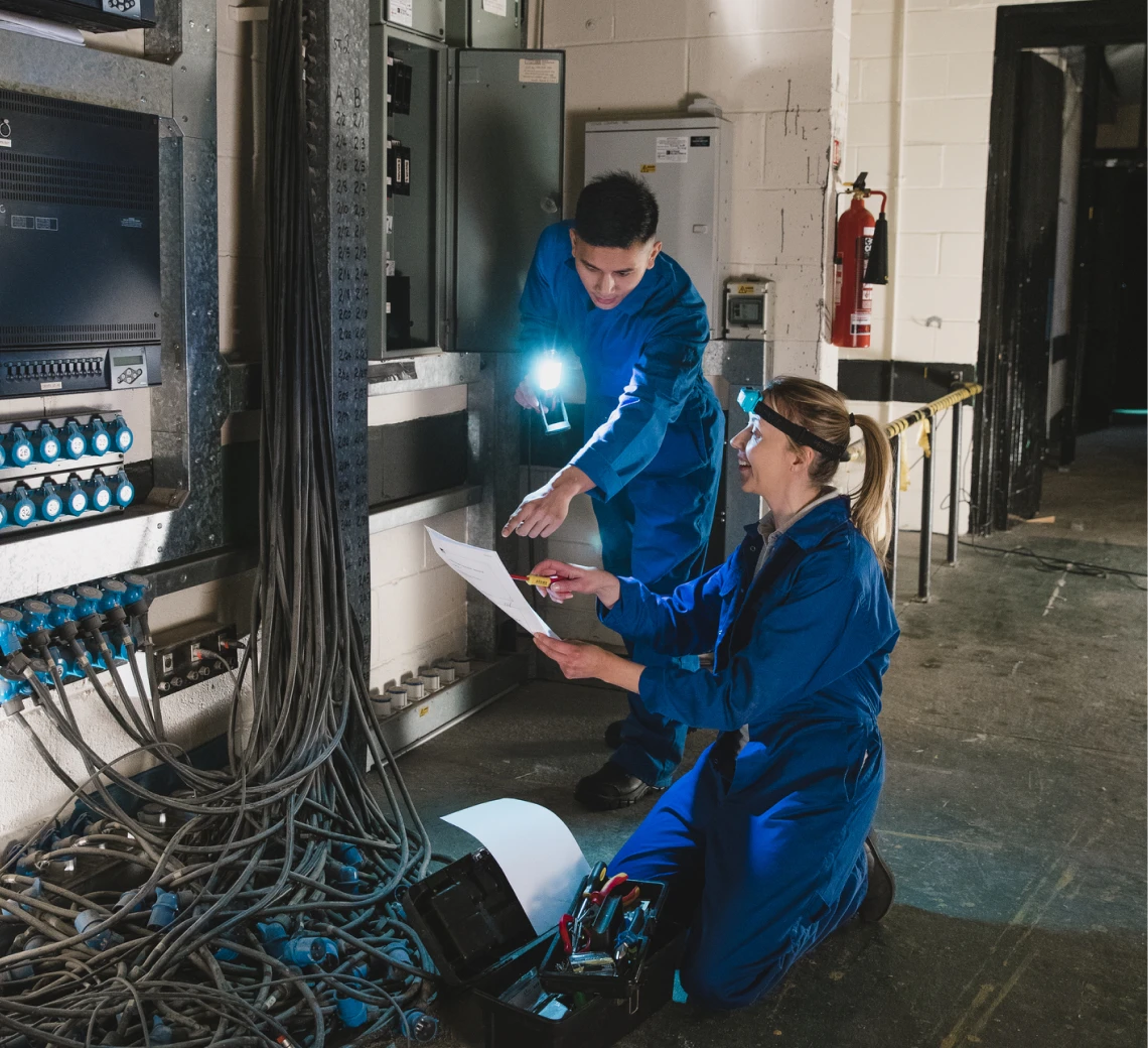 Technicians inspecting electrical panels with flashlight.