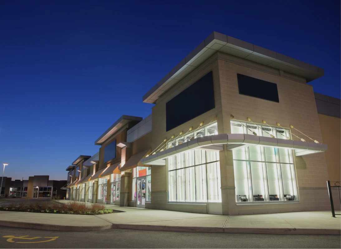 Shopping center exterior at dusk, lights on.